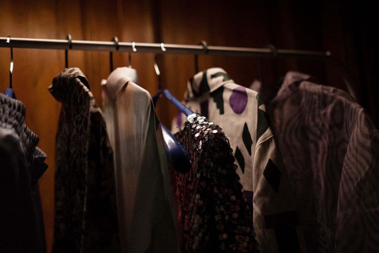A collection of stylish shirts and blouses hanging on a rod in a dimly lit wardrobe.