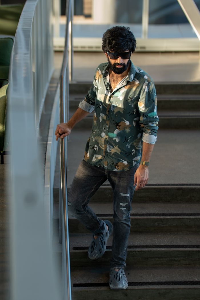 Portrait of a stylish man in a floral shirt and sunglasses, confidently descending a staircase indoors.